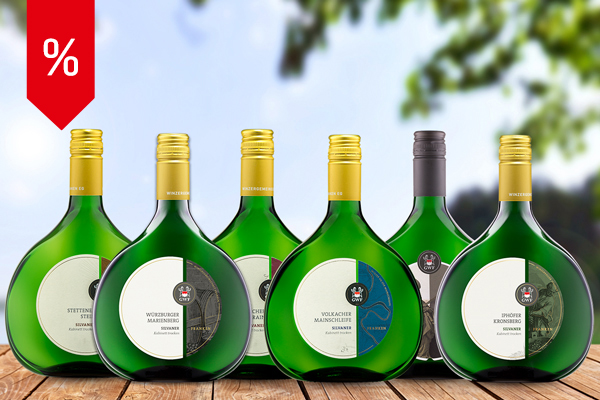 Sechs verschiedene Silvaner im Bocksbeutel aus dem Best of Silvaner-Paket vor sommerlicher Naturkulisse – blauer Himmel, grüne Bäume und Natur im Hintergrund.